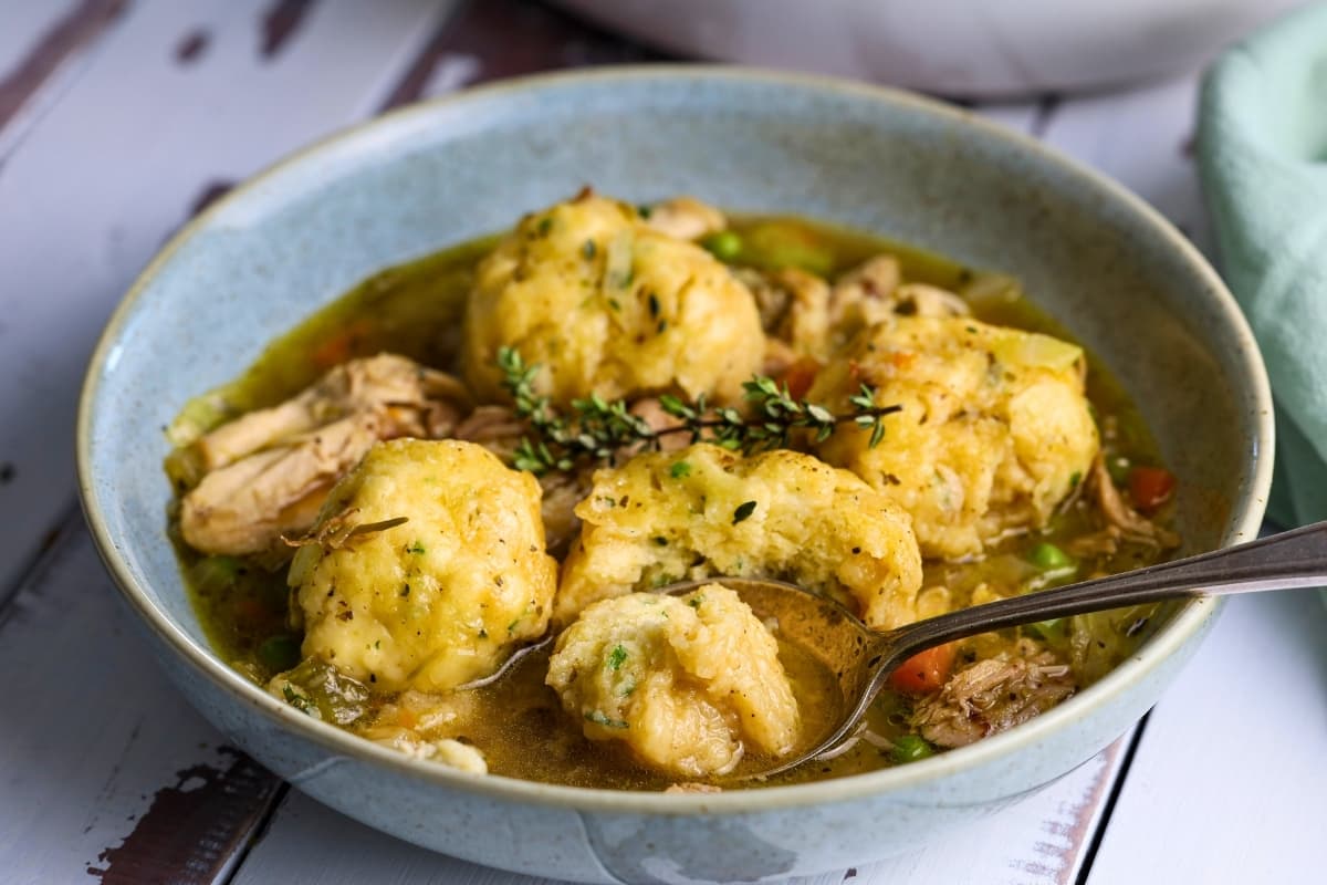 A blue stoneware bowl full of chicken and vegetable soup and topped with sourdough dumplings.