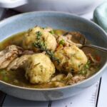 A bowl of sourdough dumplings and chicken soup garnished with fresh thyme leaves.
