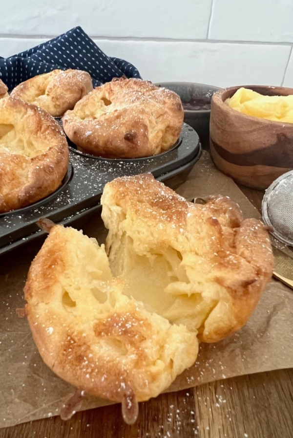 Sourdough popovers in a muffin pan. There is a sourdough popover up close that has been broken open to show the hollow interior.