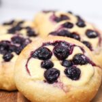 Close up photo of a sourdough brioche blueberry cheesecake roll that has just been baked. The blueberries are bleeding into the cheesecake filling.