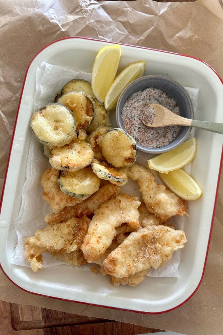 Cream enamel tray containing zucchini and chicken that has been lightly fried in sourdough discard batter. There are some lemon slices and a small dish of salt in the tray also.