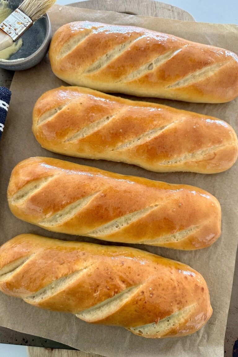 4 sourdough sandwich rolls sitting on a baking tray lined with baking paper. The sourdough subs have been brushed with butter.