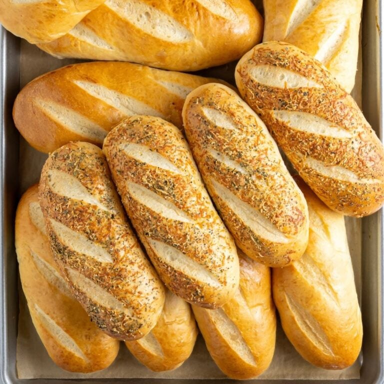A pile of fresh baked sourdough sandwich rolls on a baking sheet.