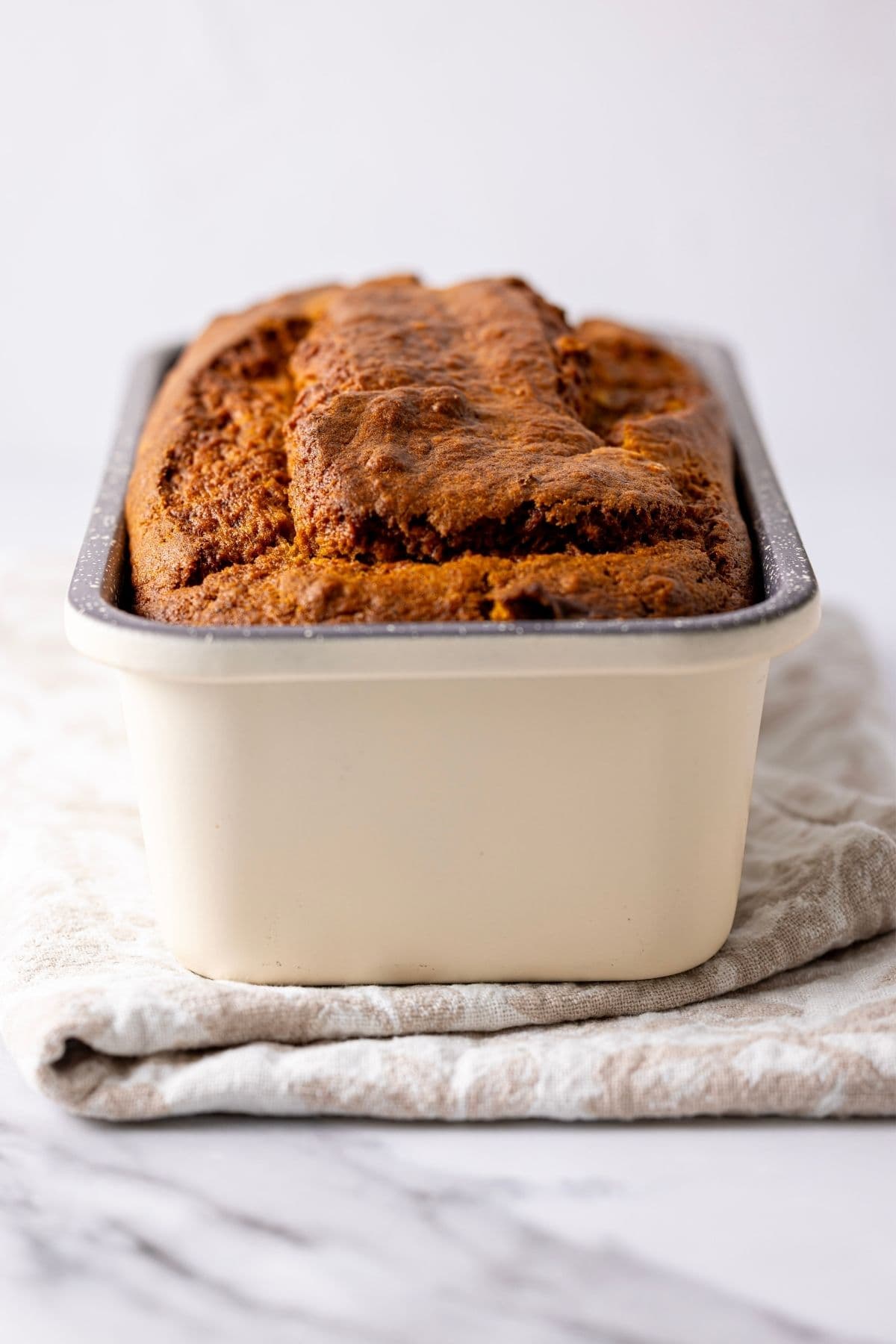 Freshly baked loaf of sourdough discard pumpkin bread cooling in a cream enamel loaf pan.