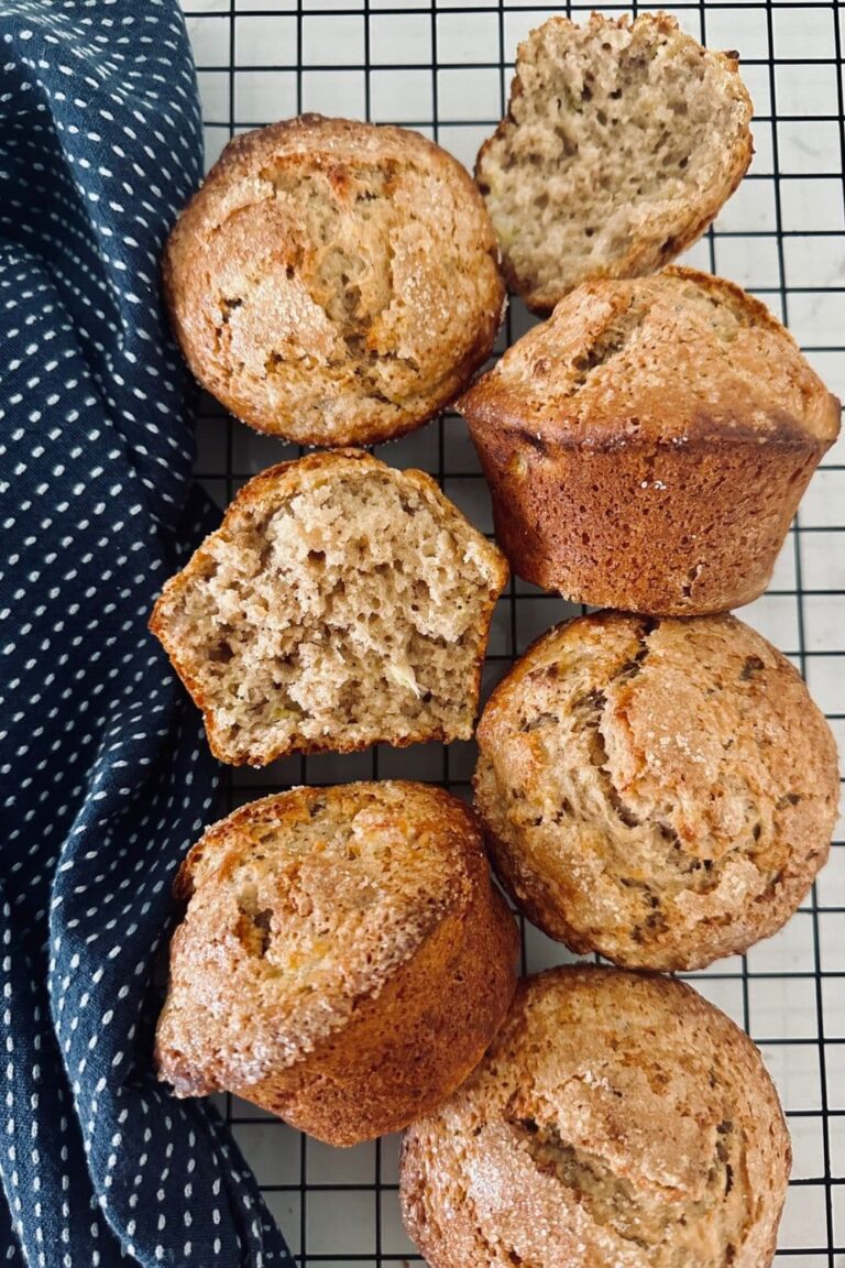 6 sourdough banana muffins sitting on a black cooling rack. There is a blue dish towel on the left of the muffins.