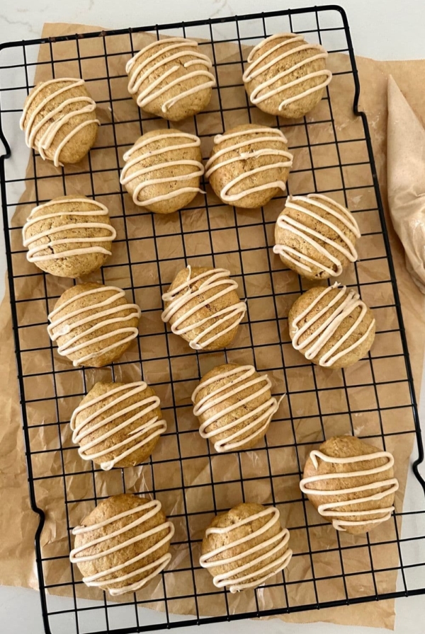 15 soft sourdough discard pumpkin spice cookies on a black wire cooling rack. There is a piece of parchment paper underneath the rack and a piping bag of glaze to the right.