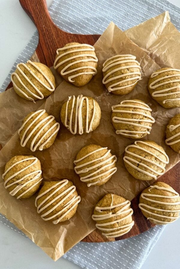 A flat lay image of a batch of soft sourdough pumpkin spice cookies laid on a round wooden board and drizzled in maple glaze.