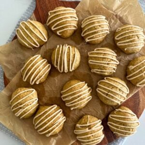 A flat lay image of a batch of soft sourdough pumpkin spice cookies laid on a round wooden board and drizzled in maple glaze.