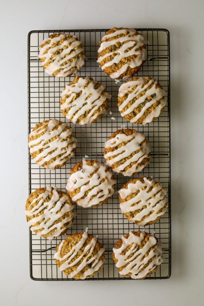 A wire cooling rack covered in sourdough oatmeal raisin cookies drizzled in stripes of simple sugar glaze.