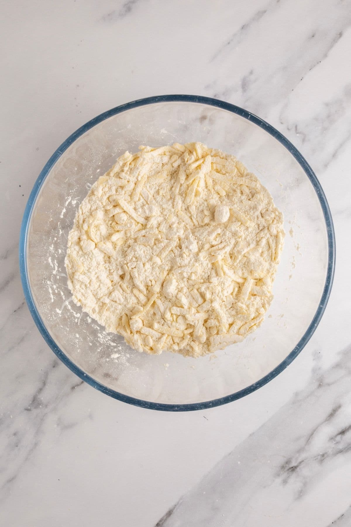 A glass bowl filled with all-purpose flour and has cold, grated butter tossed through it.