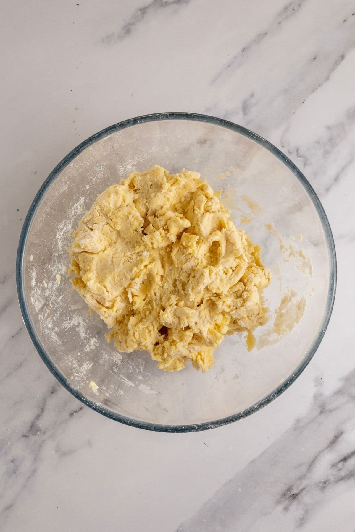 The rough dough for the pastry for sourdough pumpkin pie pushed together in a glass bowl. The pastry dough is very rough at this stage.