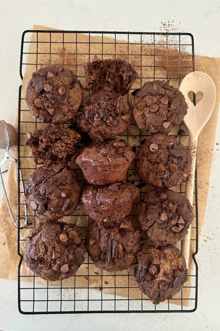 A batch of sourdough chocolate zucchini muffins sitting on a black wire rack.