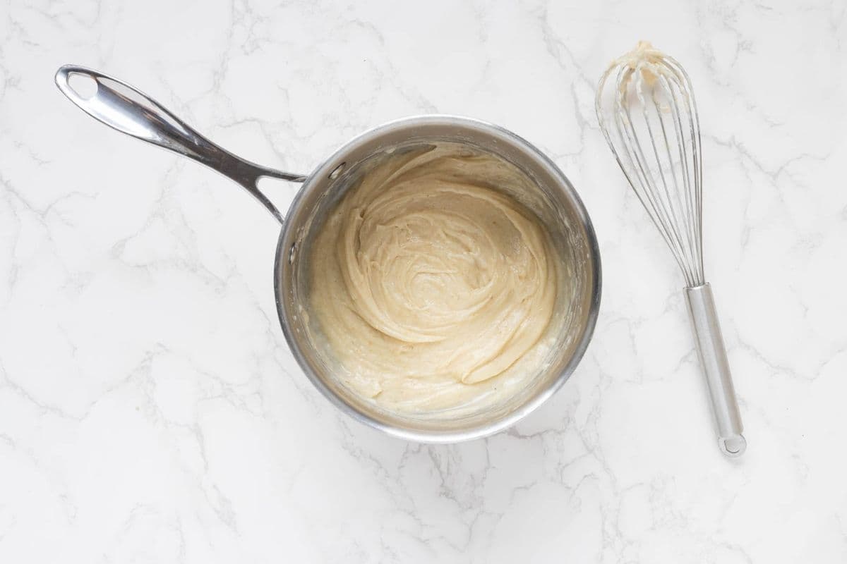 A process photo showing a saucepan with a roux that has had some milk added and whisked together to thicken.