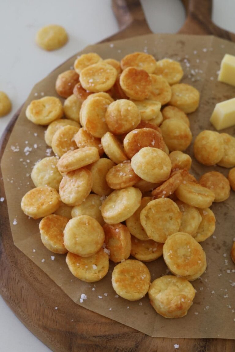 Sourdough Goldfish Crackers piled up on a wooden serving board. You can see the flaky sea salt that has been sprinkled over them.