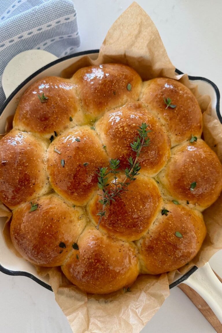 Sourdough skillet rolls bathed in honey thyme butter sitting in an enamel cast iron skillet.