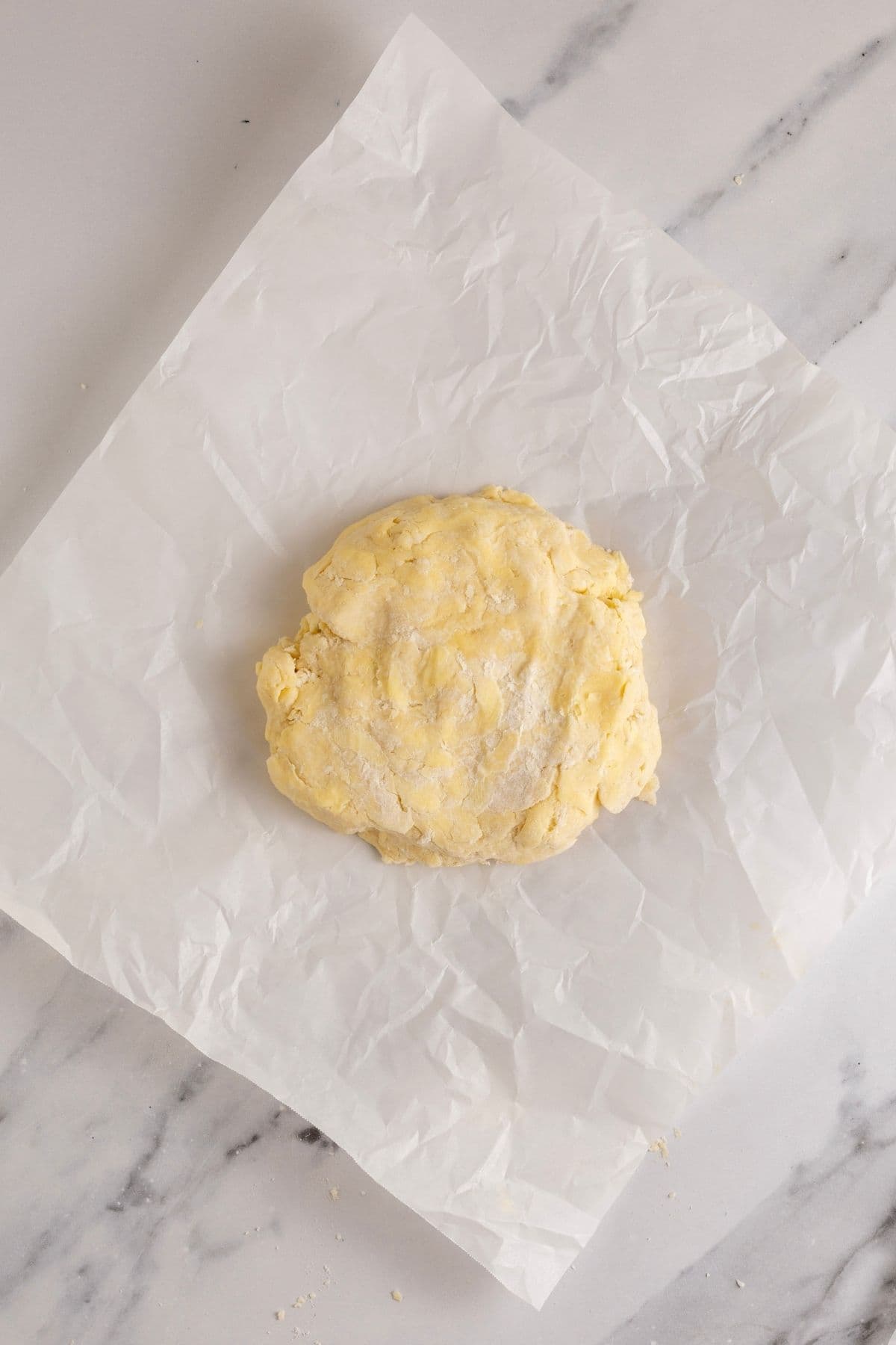 A disc of sourdough pumpkin pie pastry being wrapped in a square of parchment paper.