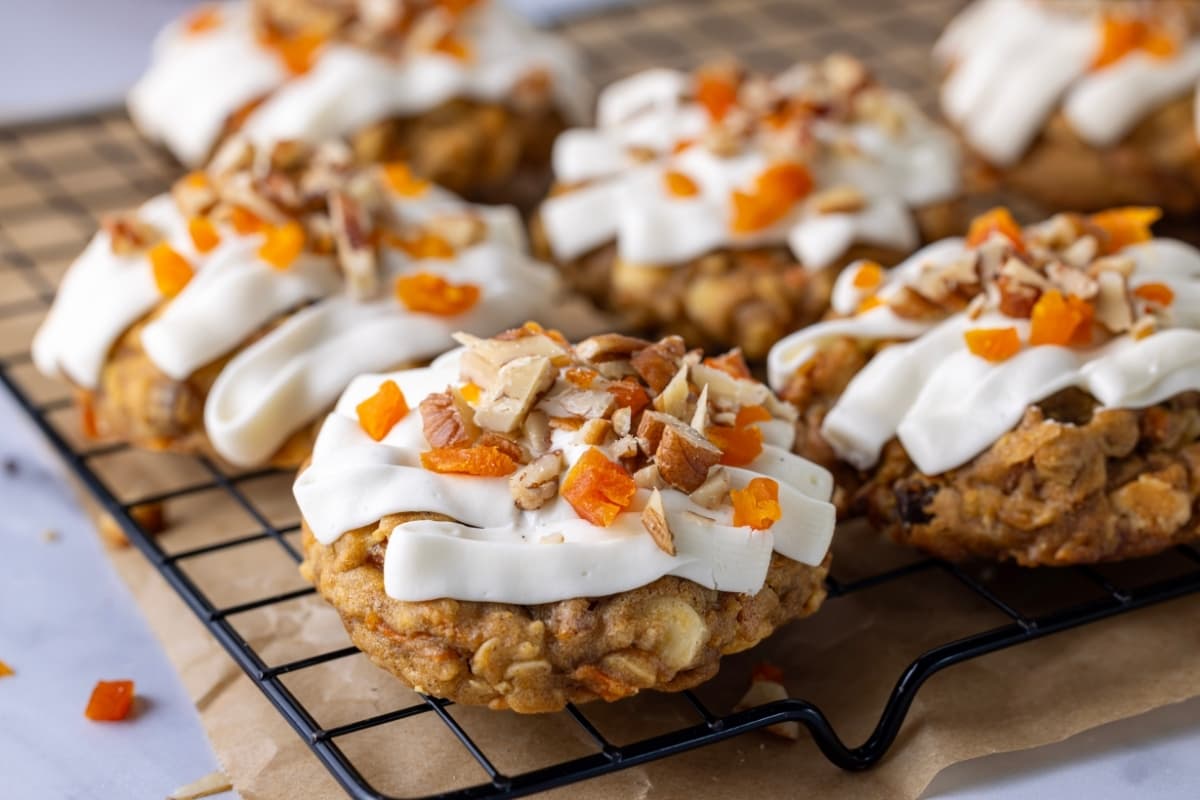 A horizontal photo of a batch of sourdough carrot cake cookies with vanilla cream cheese frosting sitting on a black wire cooling rack.