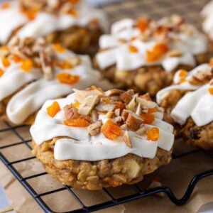A square photo of a batch of sourdough carrot cake cookies with vanilla cream cheese frosting sitting on a black wire cooling rack.