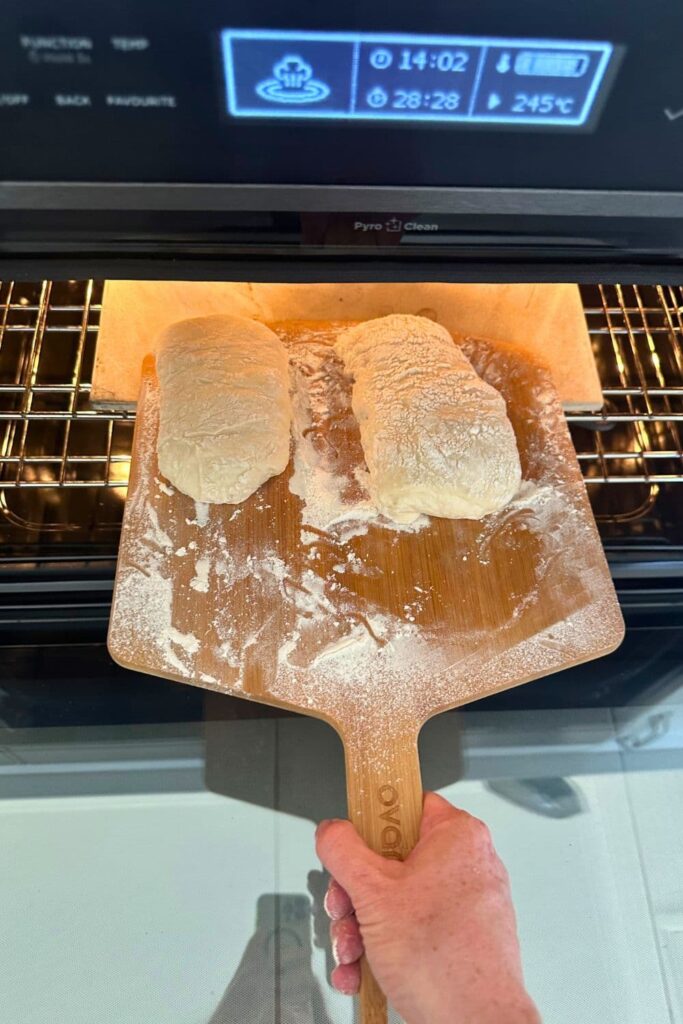 2 sourdough ciabatta rolls being loaded from a pizza peel onto a pizza stone in the oven.