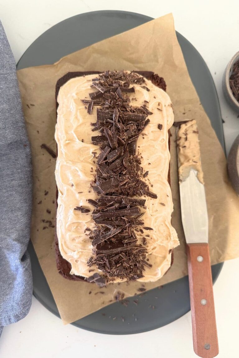 Sourdough Chocolate Chai Loaf Cake topped with chai spice vanilla cream cheese frosting and chopped chocolate. There is an offset spatula sitting the to the right of the loaf cake.