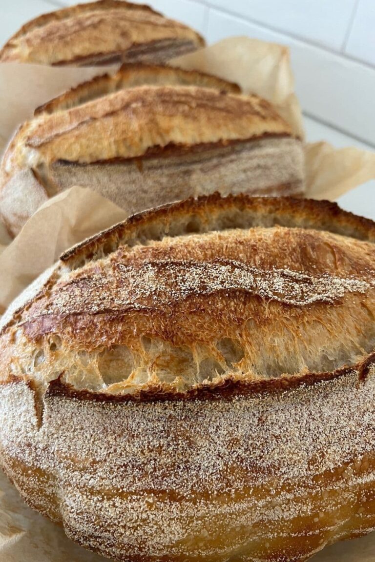 3 loaves of crusty sourdough bread sitting in a row. Each loaf has some parchment paper around it.