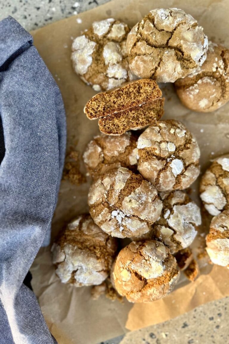 Sourdough Gingerbread Crinkle Cookies laid out on a piece of parchment paper. There is a blue dish towel to the left of the photo.