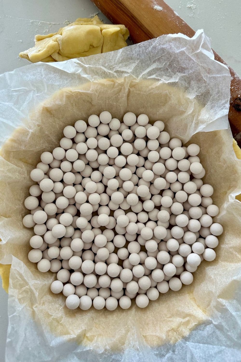 Sourdough pie crust that has been laid in a pie dish, covered in baking paper and then topped with ceramic pie weights.