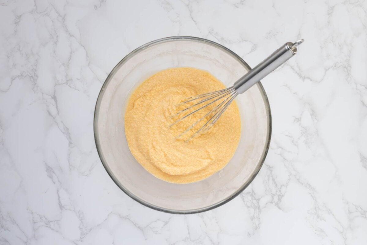 A glass bowl containing the light and fluffy wet ingredients that have been whisked together.
