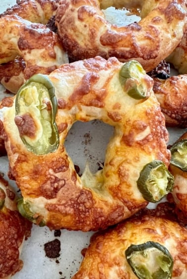 Jalape&ntilde;o Cheddar Sourdough Bagels that have just come out of the oven. The cheese is golden and crispy. There are several bagels in the photo but the main focus is on the middle one.