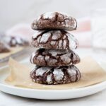 A stack of 4 sourdough chocolate crinkle cookies sitting on a small white plate lined with parchment paper.