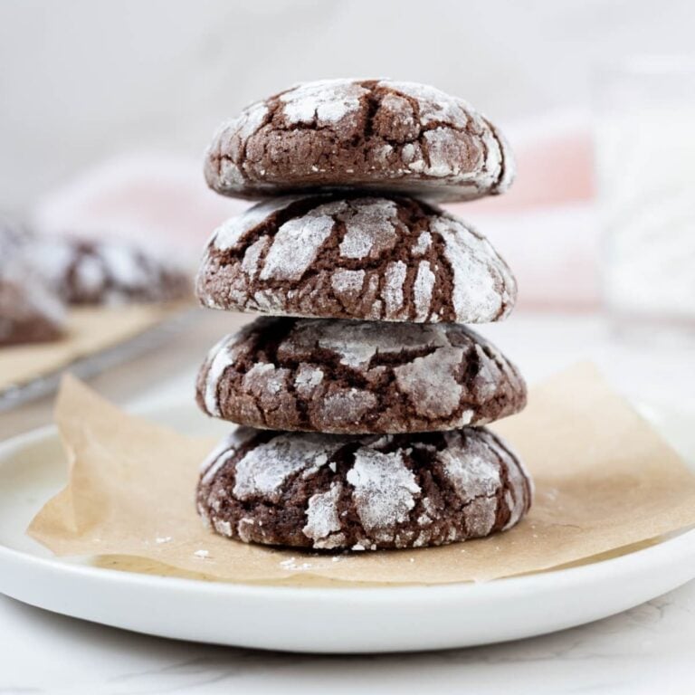 A stack of 4 sourdough chocolate crinkle cookies sitting on a small white plate lined with parchment paper.