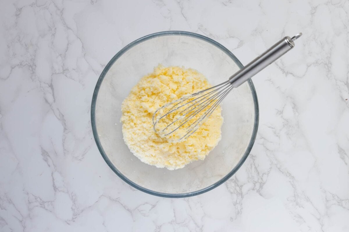 A glass bowl with butter and sugar that has been creamed together with a whisk.