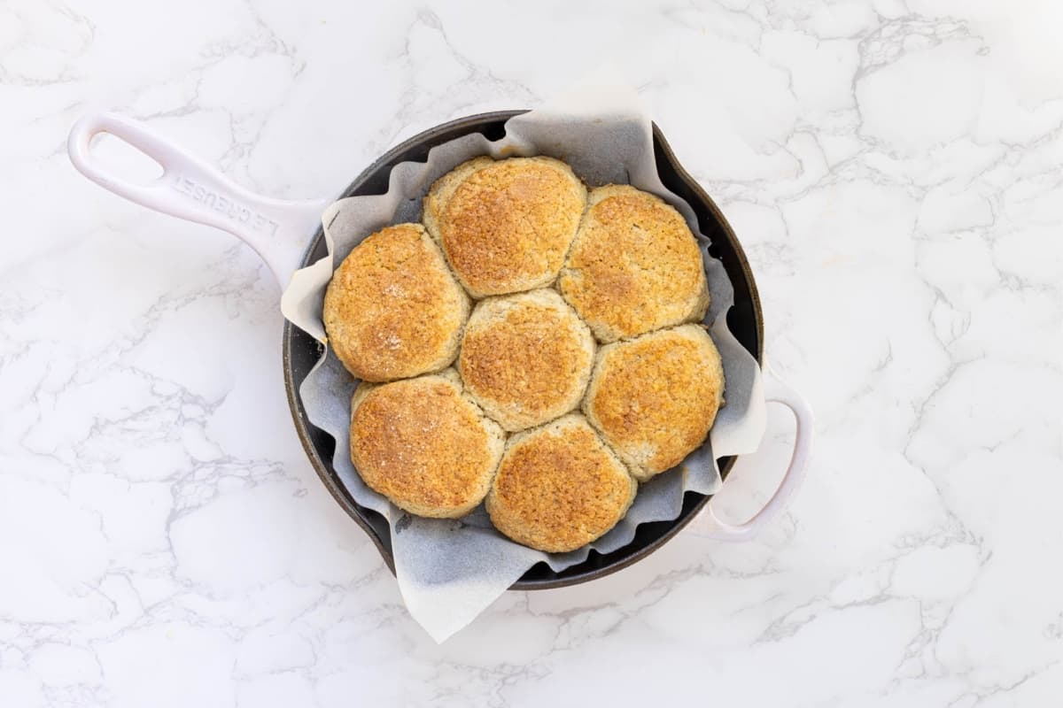 A cast iron skilled lined with parchment paper and filled with 7 freshly baked, golden brown sourdough biscuits. 