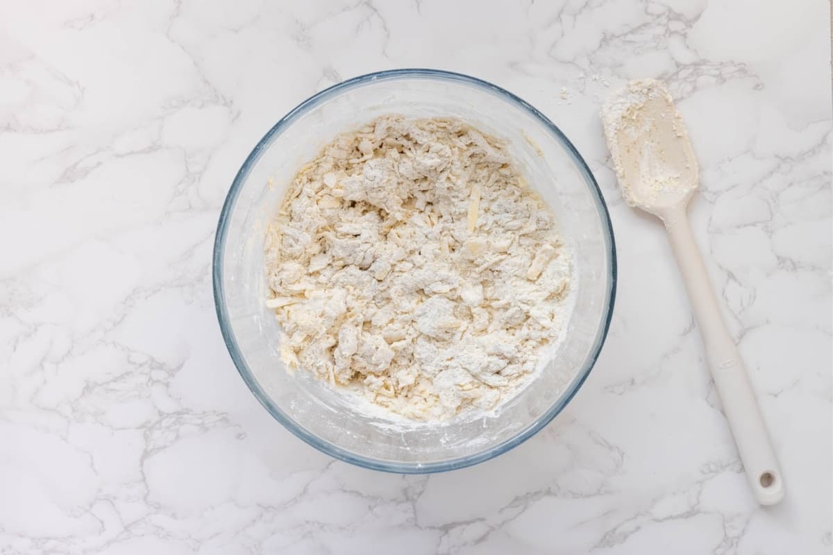A glass bowl showing the cold grated butter that has been rubbed into the dry ingredients.