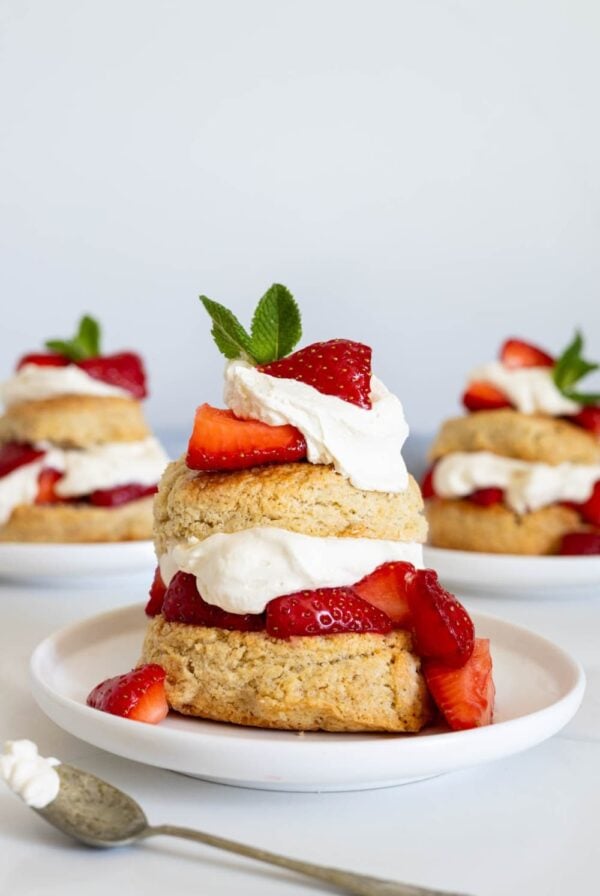 A close up image of a strawberry shortcake made with sourdough biscuits, whipped cream and juicy red strawberries. It is garnished with fresh, green mint leaves.