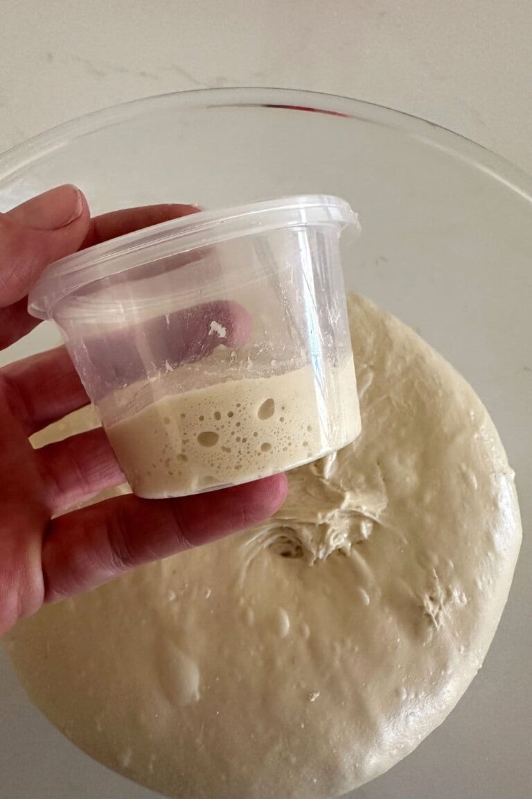 Someone holding a small aliquot jar over a glass bowl of sourdough.