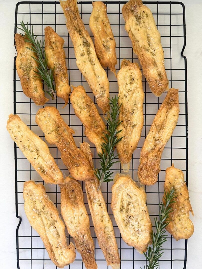 2 ingredient sourdough discard crackers sprinkled with salt and rosemary laid out on a black wire cooling rack.