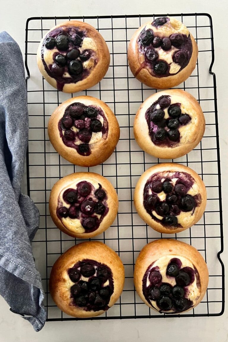 Sourdough blueberry brioche tarts with a cheesecake filling sitting on a black wire rack as a delicious sourdough discard dessert.