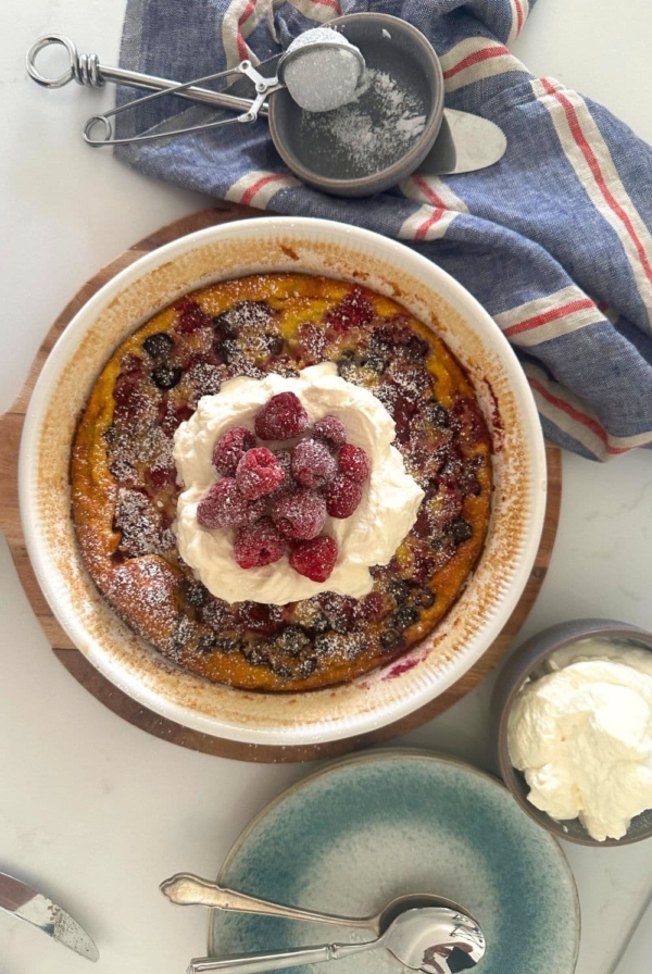 Sourdough berry clafoutis topped with whipped cream and fresh raspberries.
