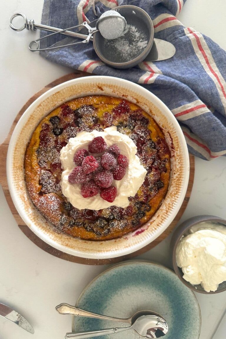 Sourdough berry clafoutis topped with whipped cream and fresh raspberries.