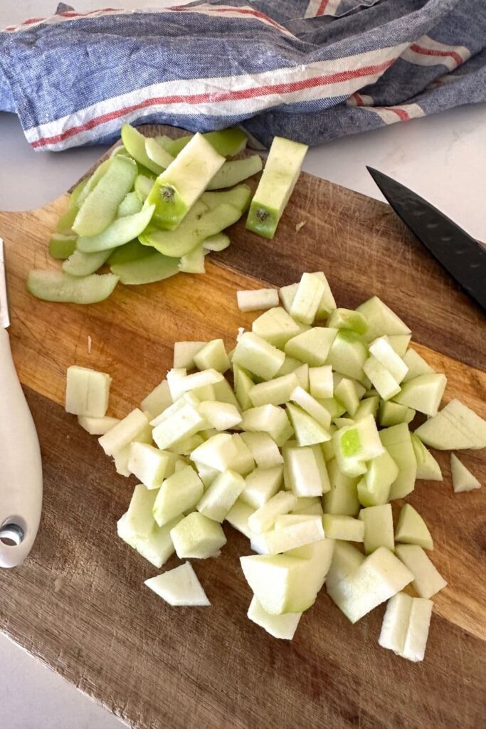 A green granny smith apple diced and set out on a wooden chopping board.