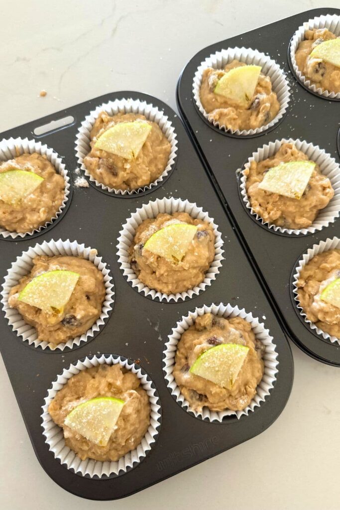 2 X 6 hole muffin trays filled with sourdough applesauce batter. Each muffin has been topped with a quarter apple slice and some sparkling sugar.
