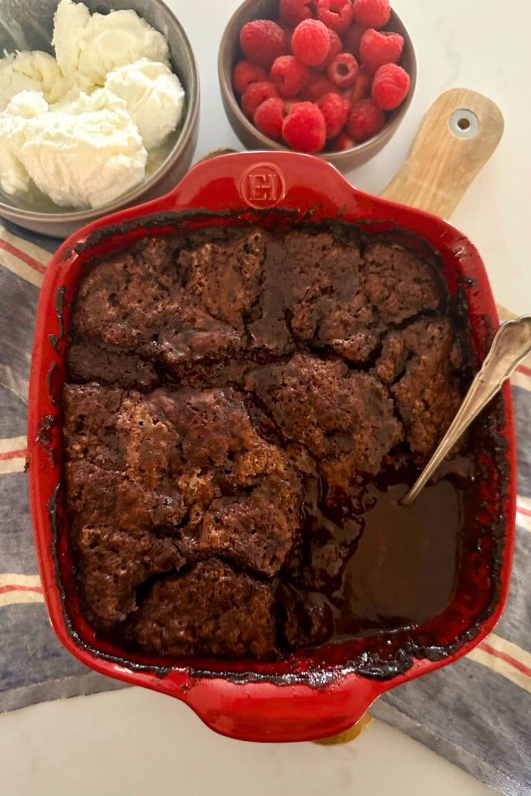 A red square dish containing sourdough chocolate cobbler served with vanilla ice cream and frehs raspberries.