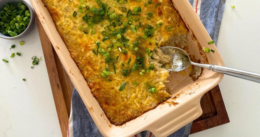 A baking dish containing sourdough hash brown casserole made with sourdough discard and potatoes. It is golden brown on top and is topped with chopped green onions.