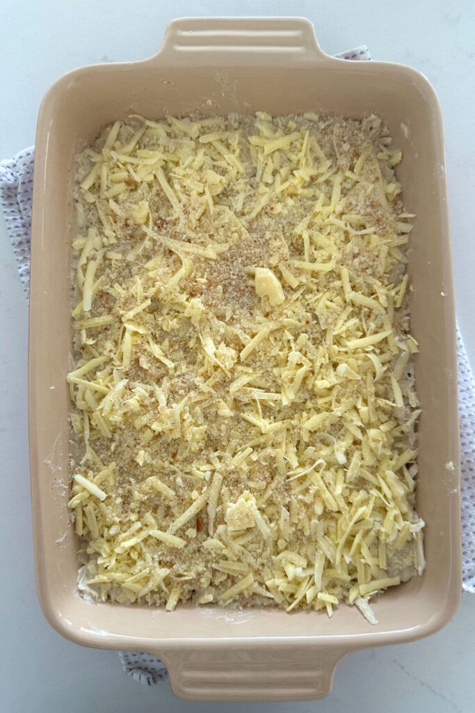 A sourdough hash brown casserole topped with cheddar cheese ready to go into the oven.
