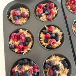 A 6 muffin hole tin filled with sourdough discard oatmeal breakfast cups topped with frozen berries and chia seeds.