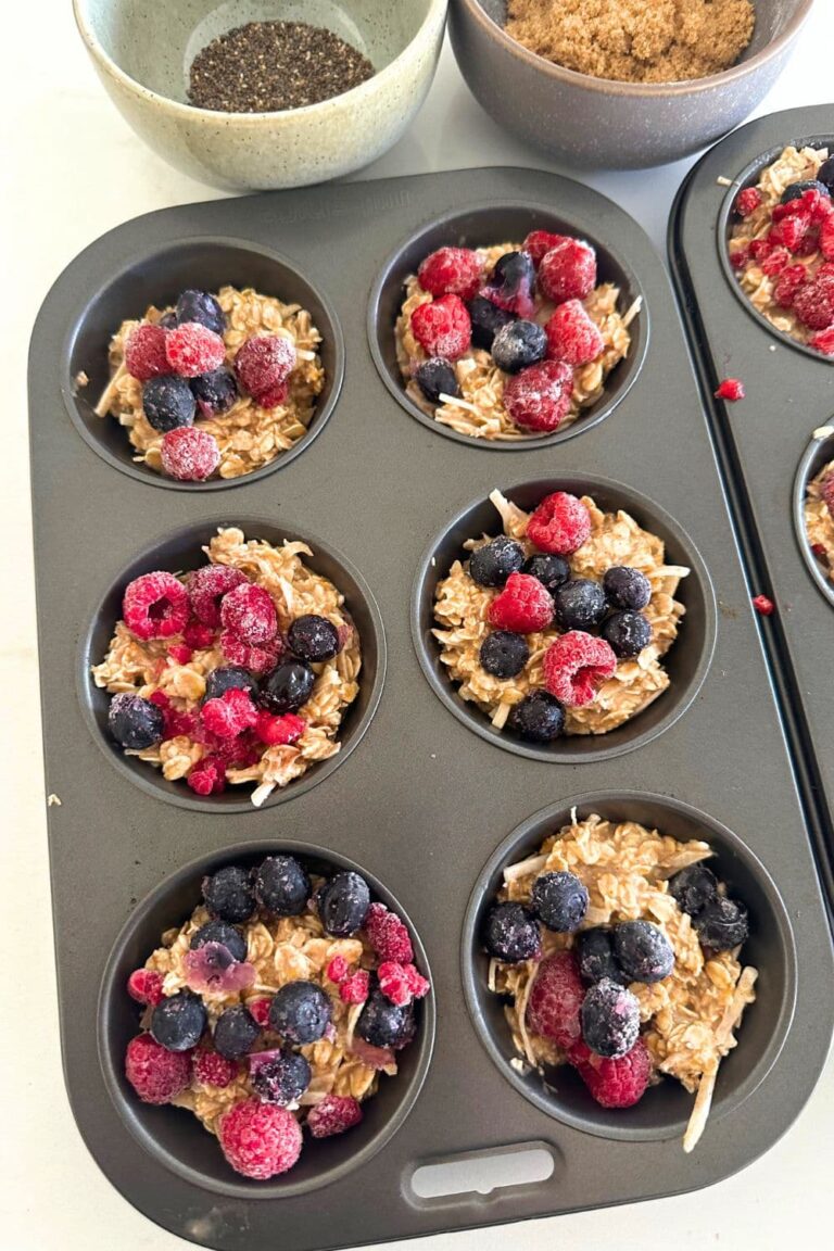 A 6 muffin hole tin filled with sourdough discard oatmeal breakfast cups topped with frozen berries and chia seeds.