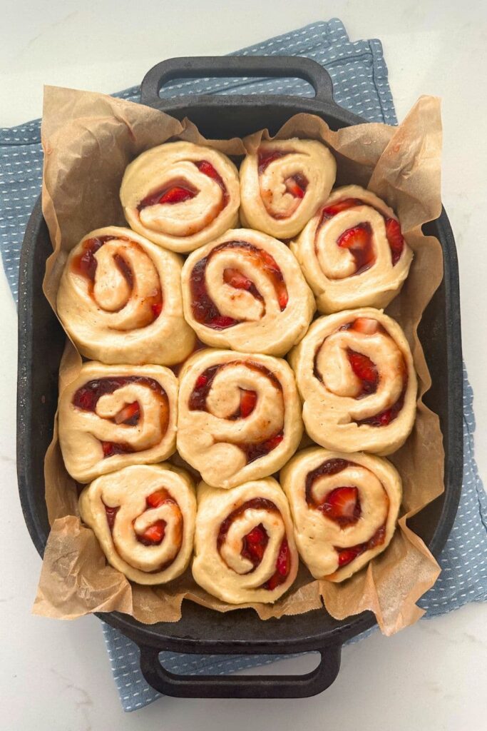 A cast iron baking dish filled with sourdough strawberry rolls that have puffed up and are ready to go into the oven.