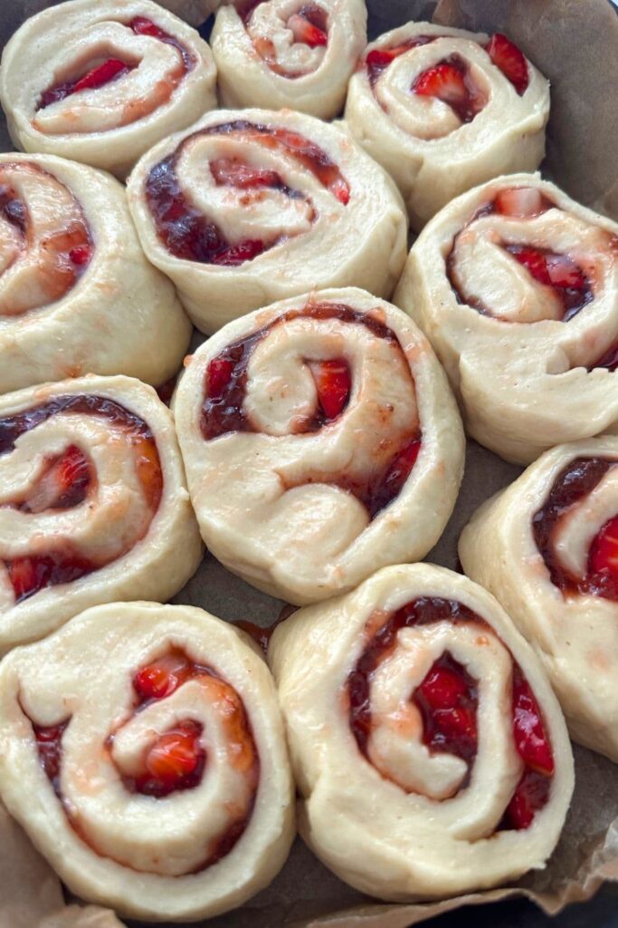 A tray of sourdough strawberry rolls that have just been rolled and placed into a cast iron dish lined with baking paper.
