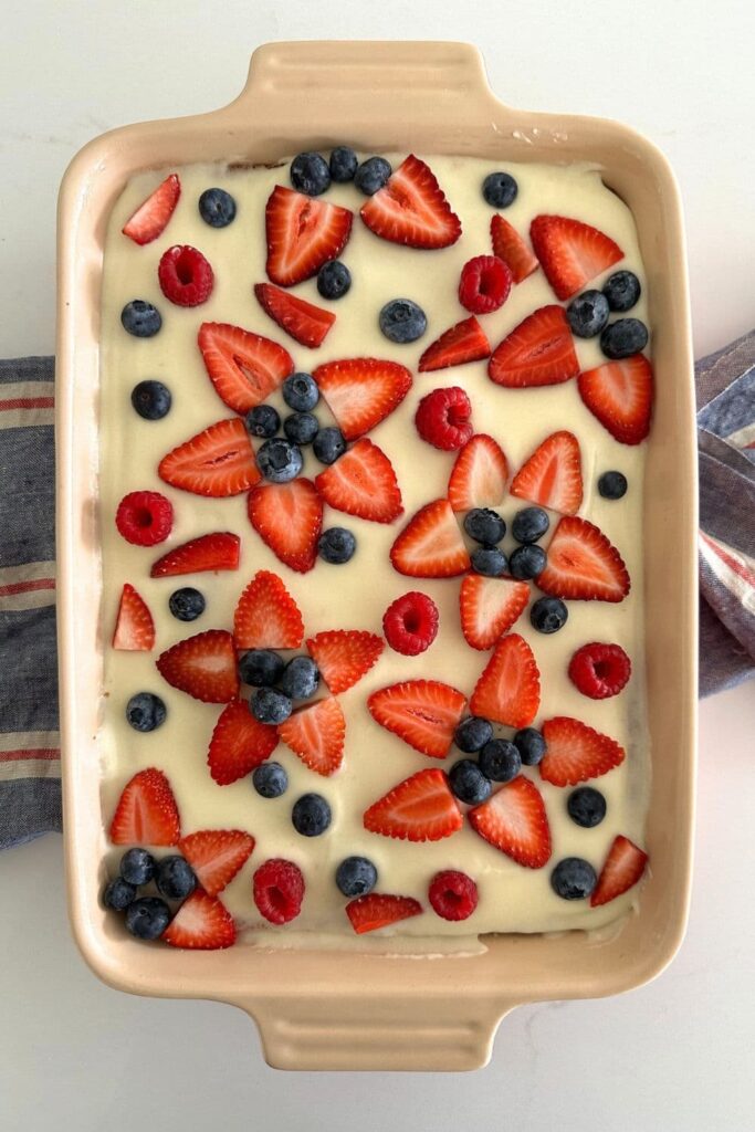 Sourdough Vanilla Sheet Cake topped with vanilla icing (white) and decorated with strawberries, blueberries and raspberries to form blue and red flowers.